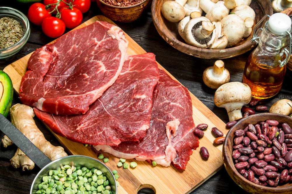 Rośliny strączkowe w cateringu dietetycznym - czy warto włączyć je do diety pudełkowej? 2 Surowe mięso obok miski fasoli, która jest idealnym roślinnym zamiennikiem białka pochodzenia zwierzęcego.
