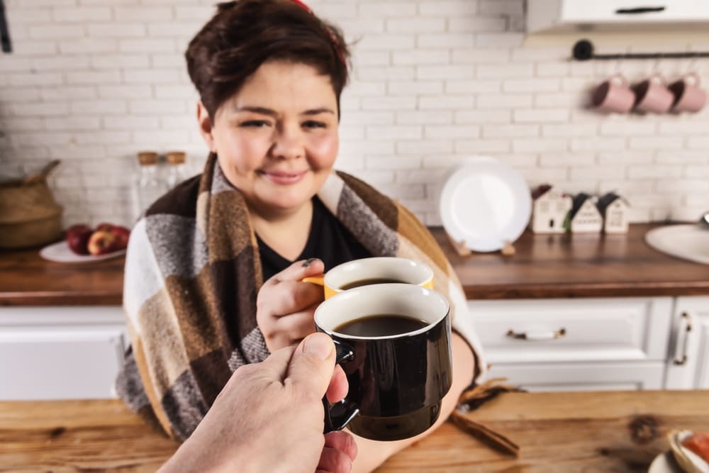 Otyła kobieta trzyma w rękach kubek z kawą. 